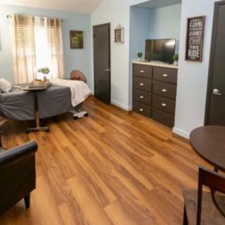 A cozy bedroom with wooden flooring, featuring a bed, dresser, and television.
