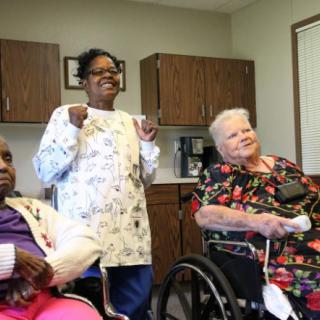 An image of seniors sitting with a caregiver in a nursing home setting.