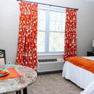A well-decorated hotel room featuring orange floral curtains, a neatly made bed, and a small table by the window.