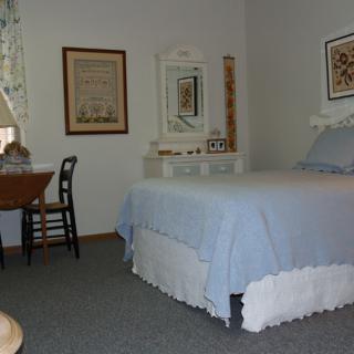 A cozy bedroom featuring a bed with blue covers, a desk with a chair, and a mirror on the wall.
