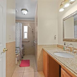 A spacious bathroom with a granite vanity, large mirror, and a tiled shower area.