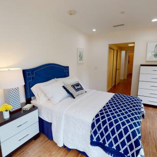 A cozy bedroom with a blue and white color scheme features a bed, nightstands, and a dresser.