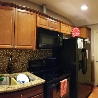 A cozy kitchen with wooden cabinets, a black refrigerator and microwave, and dishes drying on the countertop.