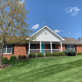 A charming house with a welcoming porch and well-maintained lawn under a clear blue sky.