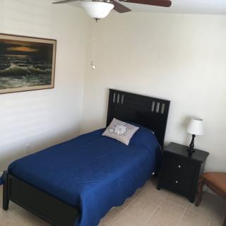 A tidy bedroom featuring a single bed with blue bedding and a nightstand with a lamp.