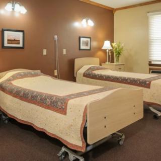 A hospital room featuring two neatly made beds with wooden frames and medical equipment.