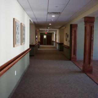 A long, empty hallway with decorative wooden columns and framed art on the walls.