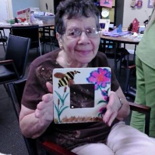 Elderly woman proudly displaying her handmade artwork in a craft room.