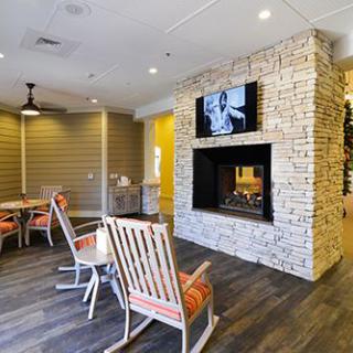 A cozy living room with a stone fireplace, rocking chairs, and a television mounted above.