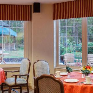 A cozy dining room with neatly set tables, offering a pleasant view through large windows.