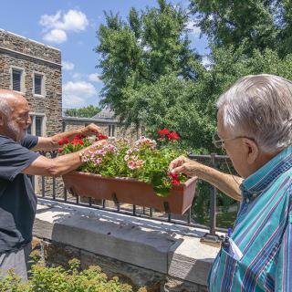 Two individuals tending to a flower box on a sunny day.