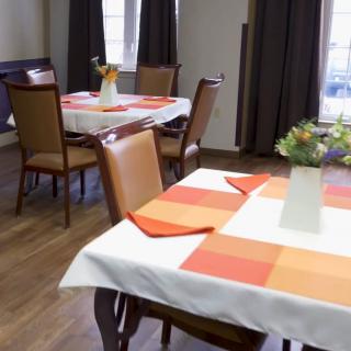 A cozy dining room with neatly set tables, featuring colorful tablecloths and floral centerpieces.