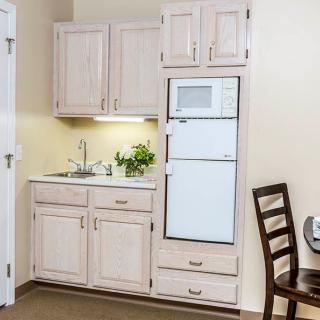 A compact kitchenette with wooden cabinets, a sink, and a built-in microwave.