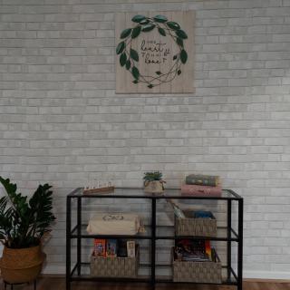 A neatly organized bookshelf with baskets, topped with decorative items and complemented by a plant and wall art.