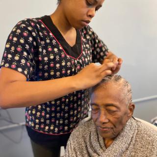 A caregiver braiding the hair of an elderly person indoors.