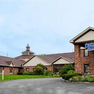 A brick church building surrounded by greenery and a paved driveway.