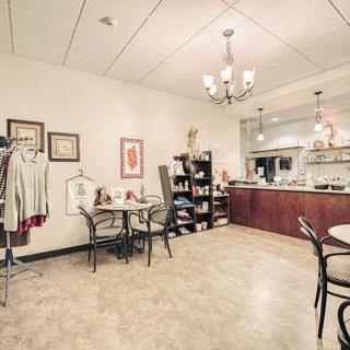 A cozy cafe interior with tables, chairs, a clothing rack, and decorative artwork on the walls.