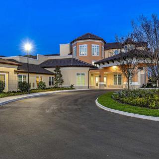 A luxurious mansion with a spacious driveway, beautifully lit at nighttime.
