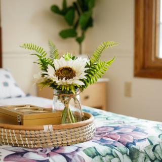 A cozy bedroom setting with a sunflower and fern arrangement in a vase on a decorative tray.
