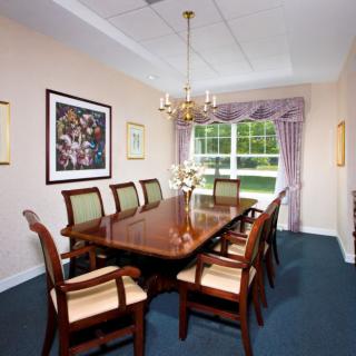 A formal dining room with a large wooden table and chairs, adorned with a chandelier and a window with draped curtains.