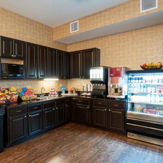 A kitchen area with vending machines stocked with snacks and beverages, featuring dark cabinetry and a hardwood floor.