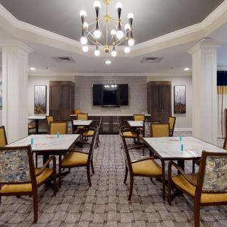 A modern dining room with tables, chairs, a chandelier, and a television on the wall.