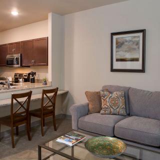 A cozy living room interior with a sofa, artwork on the wall, and a kitchen area with bar seating.