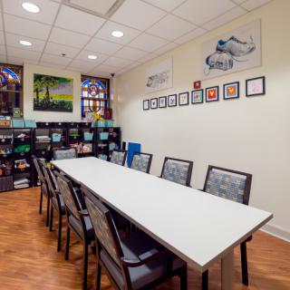 A well-organized meeting room with a long conference table, surrounded by chairs, bookshelves, and colorful artwork on the walls.