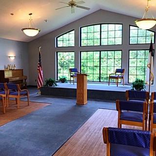 Interior of a chapel with a stage, podium, and rows of chairs.
