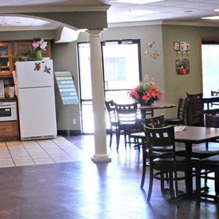 A cozy dining area with several tables and chairs, featuring a kitchen space with a refrigerator.