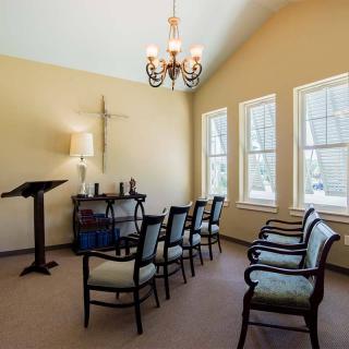 A small chapel with a row of chairs, pulpit, and cross on the wall.