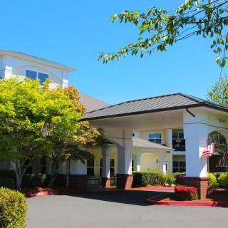 A hotel with a welcoming entrance surrounded by trees and landscaping under a clear blue sky.