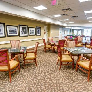 A spacious dining area with neatly arranged tables and chairs, carpeted flooring, and framed artwork on the walls.