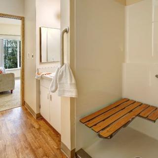 Accessible bathroom with a wooden bench and grab bar in the shower area.