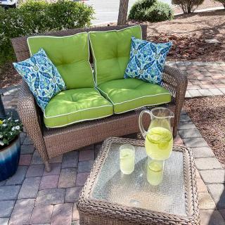 A cozy outdoor seating area with a wooden bench, bright green cushions, and a glass pitcher of lemonade on the table.