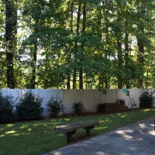 A serene outdoor space surrounded by trees, featuring a wooden bench and a white fence.