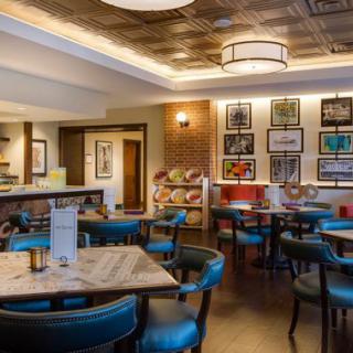 A cozy restaurant interior with blue chairs, wooden tables, and decorative artwork on the walls.