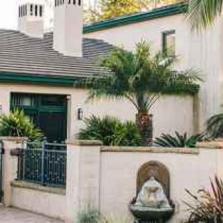 A charming house with a lush garden featuring palm trees and a decorative fountain.