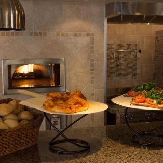 A cozy kitchen scene featuring freshly baked pizza and bread by a stone oven.