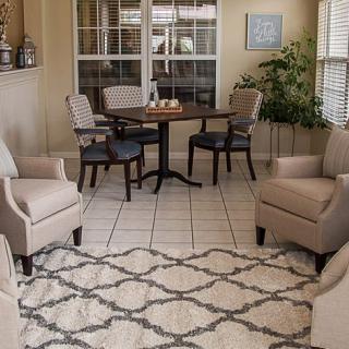 A cozy living room with a seating area, including upholstered chairs and a round table, complemented by a patterned rug and indoor plants.