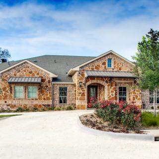 A beautiful stone facade house with a curved driveway and landscaped front yard.
