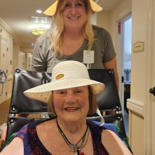 A joyful moment shared between a caregiver and an elderly woman, both wearing hats.