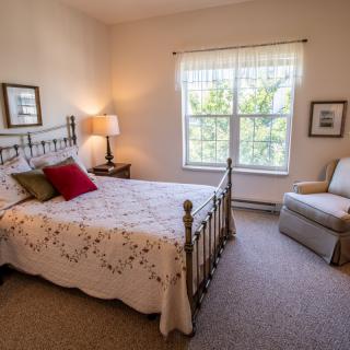 A cozy bedroom with a decorative bed, a window letting in natural light, and a comfortable chair.