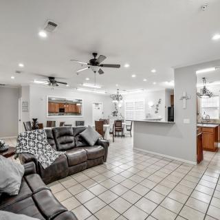 A modern open-space living room with a view into the kitchen, featuring comfortable furniture and tile flooring.