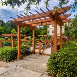A wooden pergola in a lush garden setting with a paved pathway and surrounding greenery.
