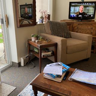 A cozy living room setup featuring a comfortable armchair, a coffee table with magazines, and a TV in the background.