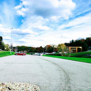 A serene view of a parking lot surrounded by lush greenery and a bright, cloudy sky.