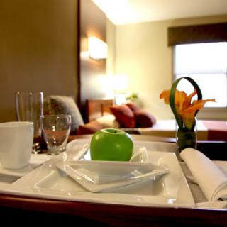 A neatly arranged room service tray featuring a green apple and flowers, set in a cozy hotel room.