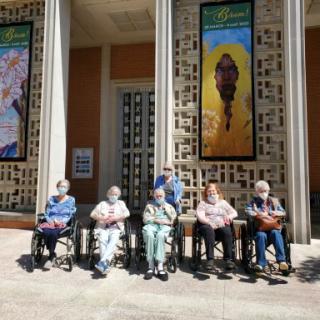 A group of elderly individuals enjoying a sunny day in front of colorful murals.