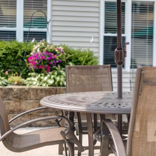 A sunny patio setup with a table and chairs, surrounded by a garden with blooming flowers.